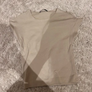 Beige ärmlös topp - Säljer en enkel och stilren beige topp med rund halsringning. Toppen är ärmlös och har en rak passform, perfekt att matcha med jeans eller kjol.