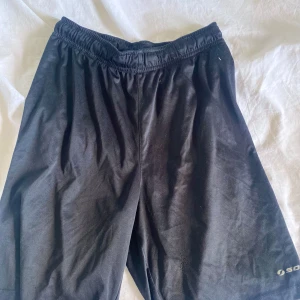 Svarta träningsshorts från SOC - Svarta träningsshorts från SOC med elastisk midja. Lätta och bekväma, perfekta för sport eller gym. Tillverkade i syntetmaterial som andas bra.