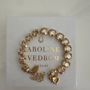 Guldigt armband med stora kristaller från Caroline Svedbom - Cora Bracelet / Golden Shadow armband med ett hjärtformat hänge. använt fåtal gånger, nypris 995kr💗pris kan diskuteras