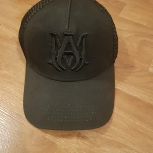 Svart keps från Amiri med mesh och läderdetalj - Säljer en svart keps från Amiri med broderad logga framtill. Kepsen har mesh på sidorna och baksidan för extra ventilation samt en detalj i äkta läder. Justerbar passform och stilren design.