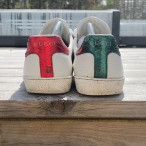 Gucci ace  - Säljer ett par vita sneakers från Gucci med klassiska gröna och röda ränder på sidorna. Skorna ligger nya på 9k säljer för 2699, pris kan ändras vid snabb affär. Perfekta för dig som vill sticka ut med stilrena och lyxiga sneakers. Endast skor med går, lite slitna men ingen värsting