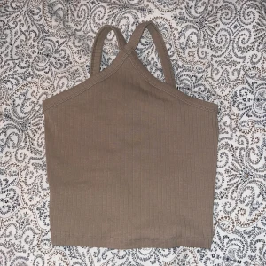 Beige ribbad croppad linnetopp - Säljer en beige ribbad croppad linnetopp med smala axelband som korsas i ryggen samt vid bröstet.