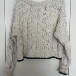 Beige stickad tröja från ZARA - Säljer en beige stickad tröja från ZARA med kabelstickat mönster och svarta detaljer vid ärmslut och nederkant. Tröjan har lång ärm och en lite croppad passform. Perfekt för kyliga dagar!