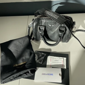 Zadig Sunny bag nano - Säljer min fina zadig väska som tyvärr inte kommer till användning. Modellen heter sunny nano studs, Dust bag och lapp ingår. Köpt i butik för 3200kr, kvitto finns. Den är i fint skick och sparsamt använd. finns lite slitningar på metalldelarna, se bild 3