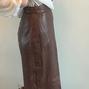 Vintage lång brun kjol - Äkta läderkjol. Har underkjol samt dragkedja bak m knapp. Högmidjad. Passar jättefint, perfekt för hösten!