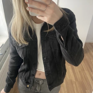 Jeansjacka - Säljer en jättefin svart croppad jeansjacka från jeansbolaget i storlek M. Den är ganska liten i storlek. Bara använd fåtal gånger, men däremot är den nedersta knappen trasig. Annars i jättefint skick⚡️köparen står för frakten!