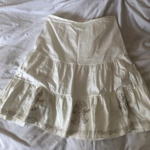 Vit broderad midikjol strl 44 - Vit kjol från Kappahl i gott skick, med broderi detaljer runt fållen. Midja: 45cm. Höft: 60cm. Längd: 70cm. Köparen står för frakt. Dma gärna vid frågor eller funderingar:)
