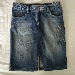 Jeanskjol - As cool jeanskjol från Vero Moda med gul-orangea broderi detaljer samt bronsfärgade runda nitar. Bra begagnat skick. Midjemått mätt rakt över: 37cm, längd: 52cm. Ingen storleks etikett men passar XS-M beroende på önskad midjehöjd🫶💕