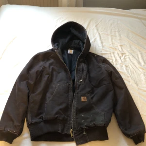Brun carharrt Jacka. - Brun carharrt jacka med fungerande dragkedja i storlek M. Bra skick med mindre vita fläckar på (går att få bort). Två innerfickor inuti jackan och tre dockar utanpå.