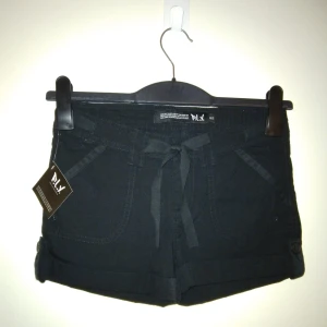 NYA och oanvända svarta korta shorts från Åhléns barnavdelning, Strlk 152 Cl / XXS. Flera fickor.  - NYA och oanvända svarta korta shorts från Åhléns barnavdelning, Strlk 152 Cl / XXS. Flera fickor. Stängs med dragkedja och knapp. Material: Lite kraftigare bomullstyg. Felfria.  Tags sitter kvar sedan inköpet. Nypris vid inköpet var 149 kr.