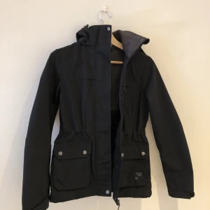 Vårjacka  - En jacka som passar till nu till våren. FINT skick och knappt använd. Med luva och spännbar i midjan 