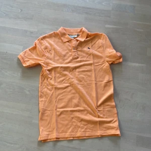 Orange pikétröja  - Den är i mjukt ganska tjockt tyg. Knappar och krage där uppe också. Aldrig använd