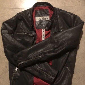 Superdry Läderjacka Large - Suuupersnygg mörkbrun skinnpaj i äkta läder från Superdry. Märken finns, dels rivmärket på axeln (se bild) men också på andra ställen, ett litet stygn där den blivit lagad på ryggen, fler bilder finns självklart!