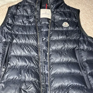 Moncler väst - Moncler väst i ovanlig modell, köpt i Tyskland för ett tag sedan, liten skada som knappt syns. Certifikat på att den är äkta samt kvitto, bag, tags allt finns med fråga vid intresse för fler bilder osv… köpt för 600€ i Tyskland nypris 800€ då den gåt