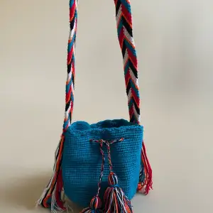 This mini bucket bag is constructed in Colombia with colorful threads made of Cotton and Aloe. The braided shoulder strap can be easily adjusted by tying a knot to shorten. Drawstring Closure with Fringed Pom Poms.  #drawstring #vintage #bucketbag 