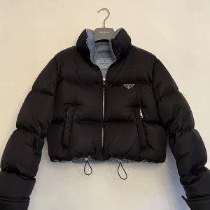 Prada Jacka - Säljer min otroliga Prada Re-Nylon cropped down jacket. Inköpt September 2022, kvitto & överdragspåse finns såklart kvar.  Mycket fint skick. Storlek 38 men skulle säga att den är liten i storleken. Nypris 23.600kr