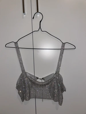 Glittrig topp - Super snygg glittrig topp i metall med strass från H&M. Änvänt 2,3 gånger o säljer pga då den kommer inte till användning. 
