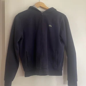 Lacoste hoodie - En väldigt snygg mörkblå hoodie från Lacoste, står att den är storlek 176 men skulle säga den sitter som S, köpare står för frakten