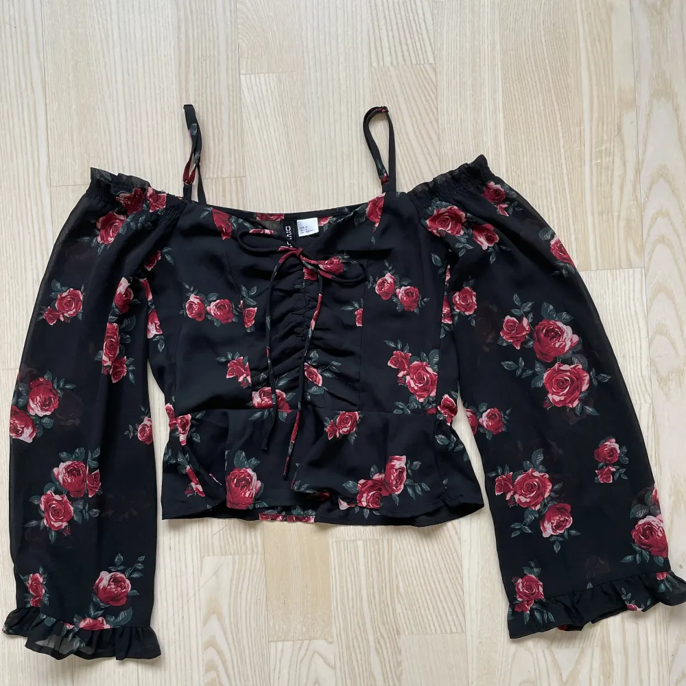 Svart blus med röda rosor från H&M. Favorittröja som tyvärr blivit för liten. Sparsamt använd.  -Stl 32/XXS - Off shoulder och croppad modell - Bra skick - Djur- och rökfritt hem. Toppar.