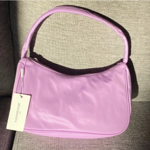 Handväska NELLY - Helt oanvänd väska från Nelly i superfin lila färg. Har tyvärr inte kommit till användning av mig så hoppas nån annan får glädje för den! Köparen står för frakt eller så kan jag mötas upp i Örebro. 