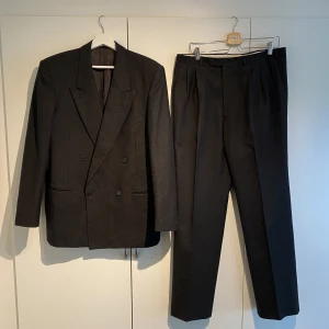 Yves Saint Laurent Dubbelknäppt Kostym - Hej, säljer en elegant mörkgrå dubbelknäppt kostym från Yves Saint Laurent. Den är i utmärkt skick och knappt använd. Enormt skönt material och grym kvalite. Liknande kostymer har nypris på närmare 40 000kr. Storlek 54 vilket motsvarar en större Large.