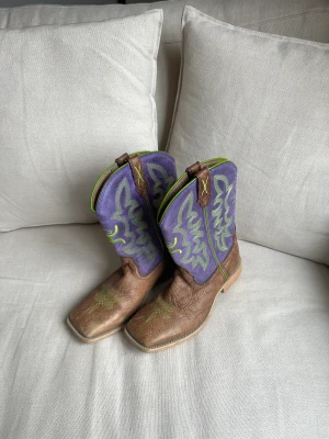 Lila/Bruna cowboy boots - Cowboy boots i fint skick. Säljer då de är för små för mig. Står att det är storlek 41, men är alldeles för små för mig som har storlek 41 normalt sett. Skulle säga att de snarare motsvarar storlek 39/40.