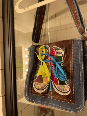 Hippieväska - Supercool väska med dekoration på som ser ut som skor (man kan knyta snörena själv). Dragkedjan som går typ runt på sidan är lite sönder (se bild tre) men den har ändå ingen funktion utan är bara för utseendet. Hör av dig om du har minsta lilla fråga!