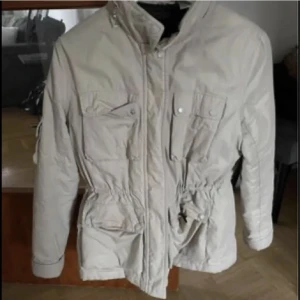 Beige jacka - Säljer en beige jacka i strl 42/44 passar båda. Finns luva på den som man kan stoppa in och dra för en dragkedja. Samt dragsko i midjan. Fint skick.