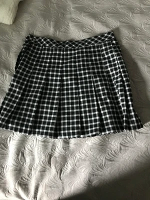 Svart/vit rutig veckad kjol  - H&M Divided Svart & vit rutig vecklad kjol.  Material: 98% Polyester 2% Elastene  Förslutning: knapp & dragkedja  Mönster: Rutig  Längd: Kort Fördel: Strechig, ser bra ut både hög midja och låg midjad, Fint mönster, Skön känsla, bra skick! Nackdel: inget