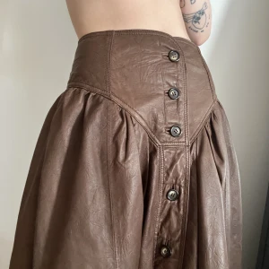 Vintage maxikjol i brun läder/skinn - Supercool vintage kjol i läder, brun med knappar och spänne i bak. Troligen high-waist, dock alldeles för stor på mig.  Har fickor!!!  Fint skick!  Uppskattar den som en S-M, men ger gärna mått. 