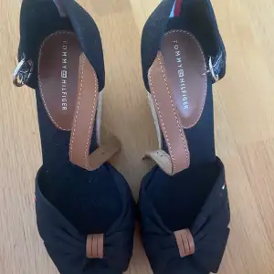 Säljer fina sandaler med kilklack från Tommy Hilfiger. Stl 37, men de är små i storleken. De är svarta med bruna skinndetaljer. Klackhöjd 9,5 cm.  Platåhöjd 2 cm  I nyskick, endast använda en gång. Nypris ca 1000 kr.
