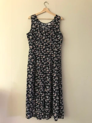 Retro klänning med knytband 90-tal - En retro sommarklänning med blommor i storlek 40. Knytband på sidorna som går att knyta bakåt eller framåt i midjan, faller fint och går knäppa med knappar hela vägen. Går att knäpp upp så att klänningen får en slits! Gott skick. 