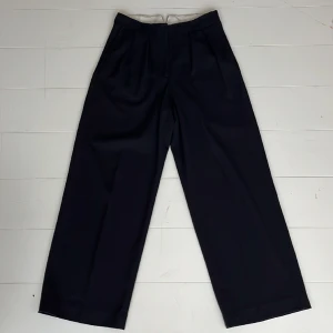 Mörkblå dressad byxa i ylle - Jätte fina blå byxor i ylle från Arket. Sköna att ha på sig. Passar både på kontoret och till mer festliga tillfällen. Fin kvalitet som håller länge. Som nya. Raka, vida ben med tyg somm faller fint och hög midja. Innerbenslängd 74 cm. 