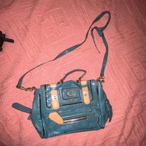 Guess blå/turkos handväska  - Blå/turkos stockholmsstils handväska med beiga detaljer från Guess, säljer för den inte kommer till användning men bra skick! 