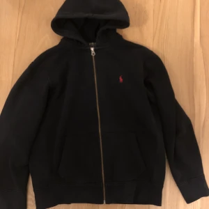 POLO RALPH LAUREN ZIP HOODIE - Äkta ziphoodie från Ralph lauren i storlek L, passar även M. Bra skick men snörena har dragits ut. Värt att notera att den även har två väldigt små hål vid kanterna av fickan men de är nästan omöjliga att se. Priset är inte hugget i sten så kom med bud.