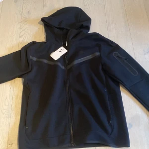 Nike tech fleece - Nike tech fleece hoodie svart. Nypris 1350kr, JD Sports i butik. Aldrig använd så 10/10 skick. Prislappar/tags kvar på tröjan.