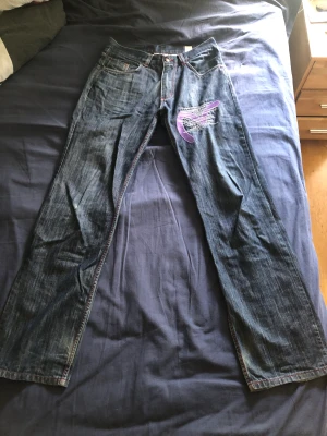 Evisu Jean - Ett Par lila evisu jeans, jag har storlek 32 och är 186 cm. Den passar mig perfekt. Dom är lite slitna på botten men det är inget man märker när man har på sig dom. Just denna modellen är svår att hitta, speciellt för ett bra pris. Unisex