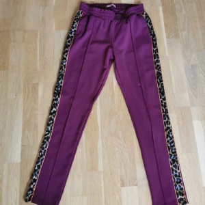 Vinröda kostymbyxor från Scotch and Soda  - Ursnygga vinröda konstymbyxor med leopardmönster på sidorna. Färgen syns bäst på sista bilden. Har snörning i midjan och sidofickor. Knappt använda, nyskick!  Storlek: midja: 33 cm och innebenslängd: 73 cm.   63% viskos, 33% nylon-polyamid och 4% elastan.