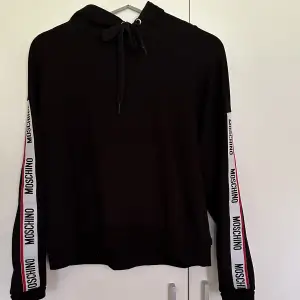 Moschino hoodie i svart med logo på ärmarna. Något kortare i modellen. Storlek xs, passar en s också.  Använd fåtal gånger, i nyskick! Nypris omkring 2200kr. 🤩