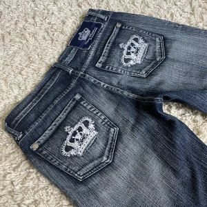 Utsvängda Victoria Beckham jeans - Äkta Victoria Beckham jeans. ❤️ Lågmidjad och bootcut modell med kronor och rhinestones där bak. Innerbenslängd: 75cm, midjemått rakt över: 39cm. Är 165cm, kan fixa fler mått! 🫶 Håll koll på min profil, lägger för det mesta upp vintage jeans! 😍