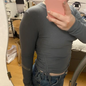 En fin mörkgrön tröja med dragsko  - En ribbad mörkgrön tröja (ser grå ut på bilden men är grön) med två dragskor på varsin sida i strl M. 