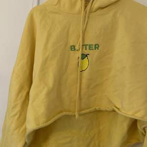 Kort hoodie i gul med ”bitter” som tryck.  Slutar under bröstet. 
