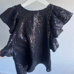 Paljett topp - Svart topp med paljetter. Volang ärmar. Storleken är 14 år men passar en XS. Fint skick. 
