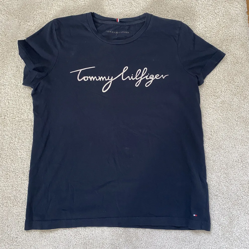 Säljer min marinblåa Tommy Hilfiger t-shirt då den inte kommer till användning längre. Den är använd några gånger, färgen på texten har slitits av lite från tvätten som man kan se på andra bilden men inget men tänker på. Köparen står för frakten! 💙. T-shirts.