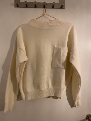Vit stickad tröja - Stickad vit tröja i tjockt material. Fin ficka på bröstet, i bra skick.