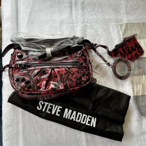 Steven Madden väsa CROSSBODY BAG BLACK/RED - BGLOW-G CROSSBODY BAG BLACK/RED  Helt ny, använd en gång, Så fin väska, fin present. Säljes med dustbag samt tag. Orderbekräftelse kan visas för att garantera äkthet.  Väskan är i stil med balenciagas väskor, liknar dom, modell city bla