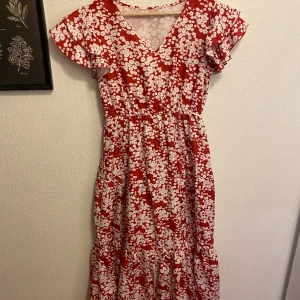 Sommarklänning - En röd fin sommarklänning med vita blommor! Volangärm och resår i midjan. Oanvänd. Storlek M. Finns på andra sidor också 🥰