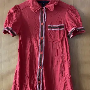Röd kortärmad skjorta med bruna och vita detaljer. Något puffade ärmar, storlek XS (Sorry har ingen ångare så den är skrynklig på bilderna! )