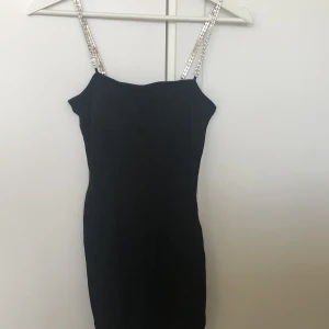 Svart cool klänning - Svart klänning i storlek XS med axelband i plast. Har en mindre slits  vid vänster ben. Väldigt kort för mig som är 160cm. Endast använd nyårsafton 2020.