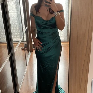 Balklänning - Super fin balklänning i en mörkare grön färg. Klänningen är i storlek S och har en hög slits längs högra benet. Materialet är super fint och klänningen har vikt i sig. Klänningen är köpt på lovelemonadeonline.com för 2500kr. Endast använd 1 gång. 
